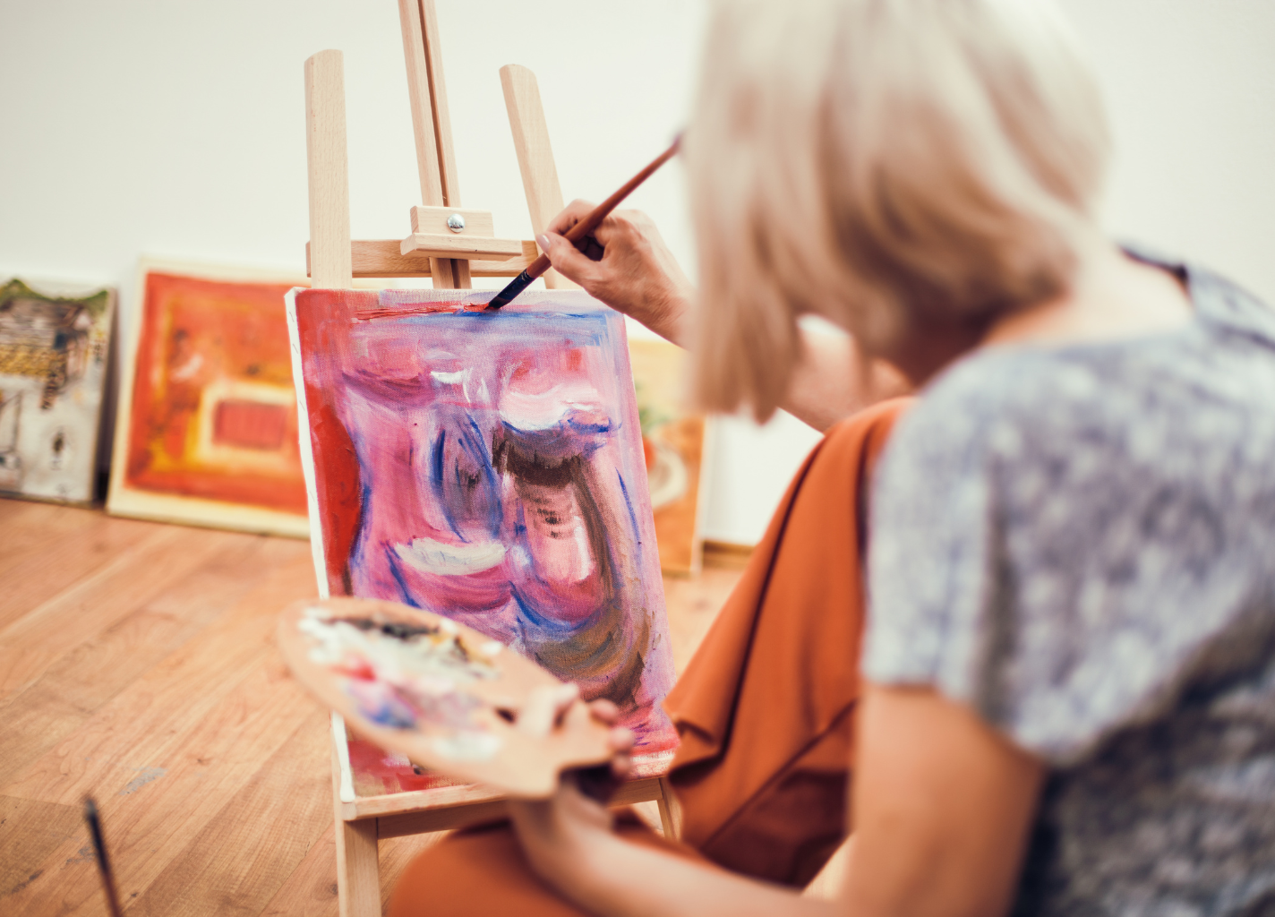 Kobieta siedzi przed sztalugą i maluje martwa maturę.