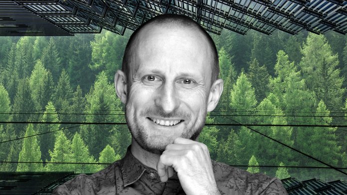 Uśmiechnięty wizerunek profesora Jakuba Kronenberga na tle zielonych drzew, widoczne również szklane fasady drapaczy chmur