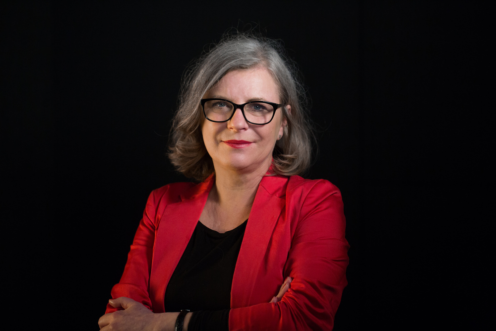 A portrait photo of Prof. D. Merecz-Kot wearing a red jacket against a black background