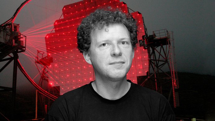 Profesor Julian Sitarek na tle rozświetlonego czerwonymi laserami teleskopu czerenkowskiego