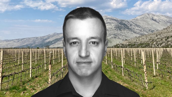 Dr Marek Majer na tle pola krótko przyciętych winorośli. W oddali góry.