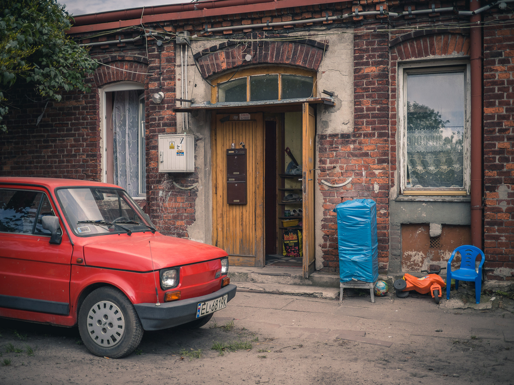 na zdjęciu widać fragment niskiego budynku z cegły i auto mały Fiat