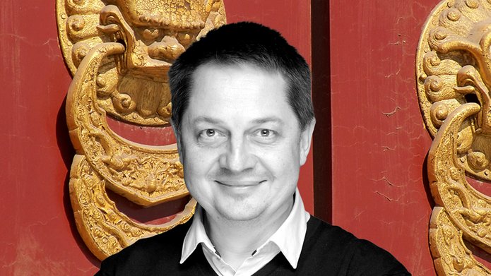 Czarno-biały wizerunek profesora Mierzejewskigo w czarnym swetrze z widocznymi spod niego białymi kołnierzykami, w tle dwie duże złote, azjatyckie płaskożeźby w kształcie kołatek do drzwi