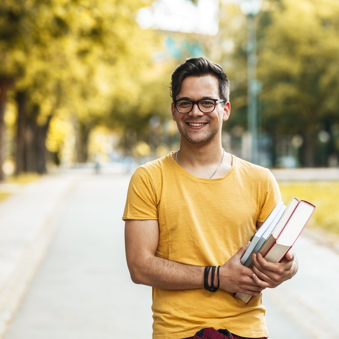 Young male student standing at the college yard.He holding a boo Male student