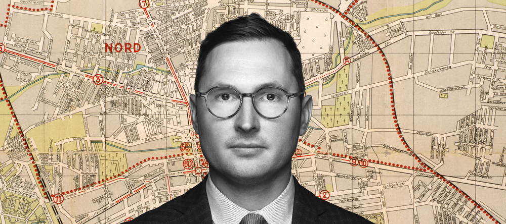 Dr Adam Sitarek na tle fragmentu mapy łódzkiego getta